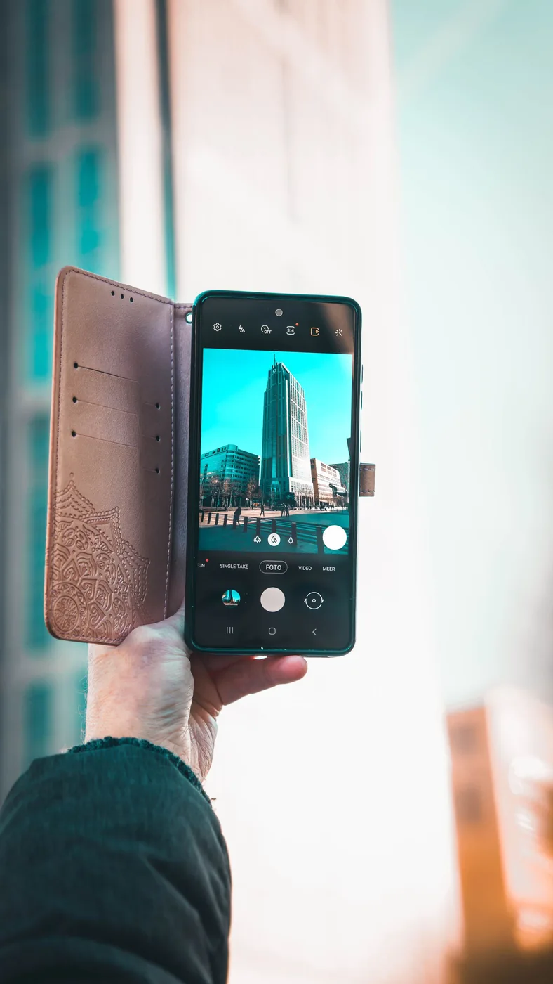 Person using a smartphone to photograph tall buildings on a city street