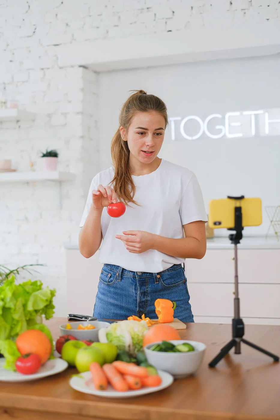 Woman preparing vegetables while recording with a smartphone on a tripod in a kitchen