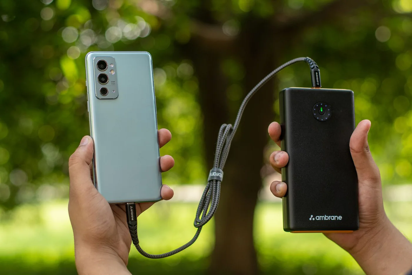 Hands holding a phone connected to a portable power bank outdoors