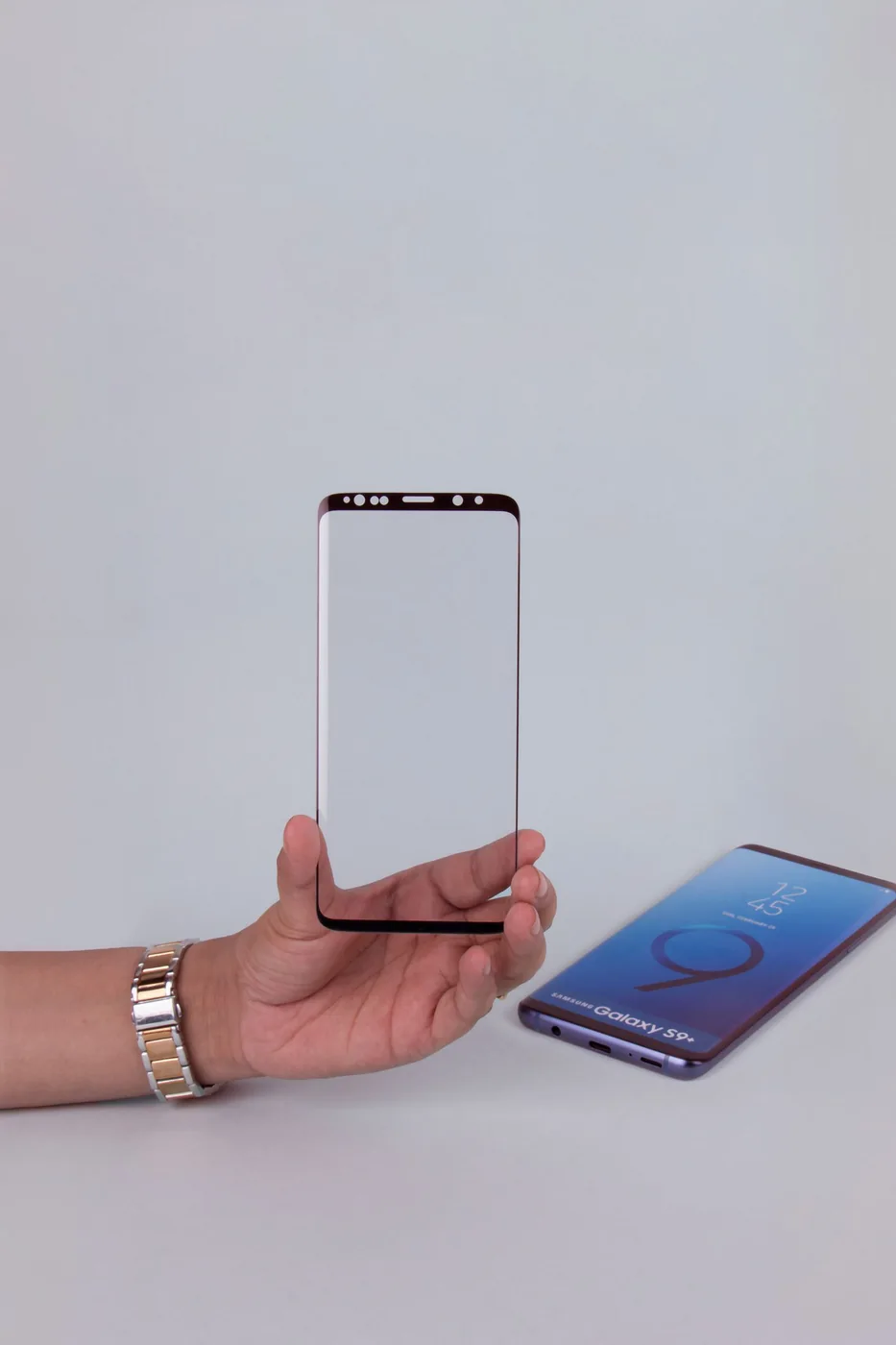 Hand holding a transparent glass screen protector beside a smartphone