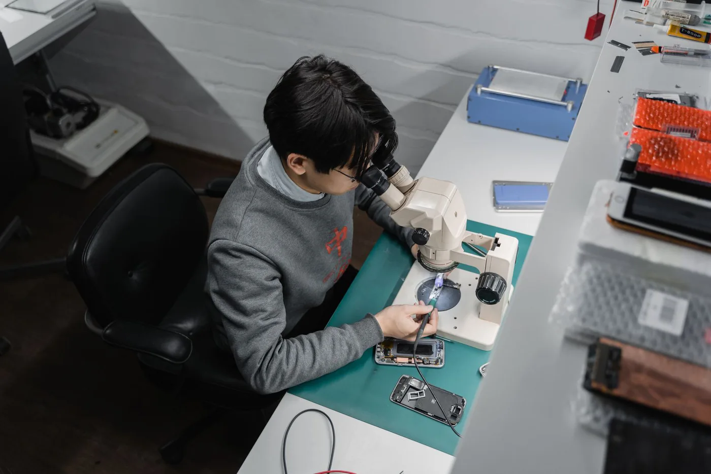 Technician repairing a smartphone under a microscope at a workbench