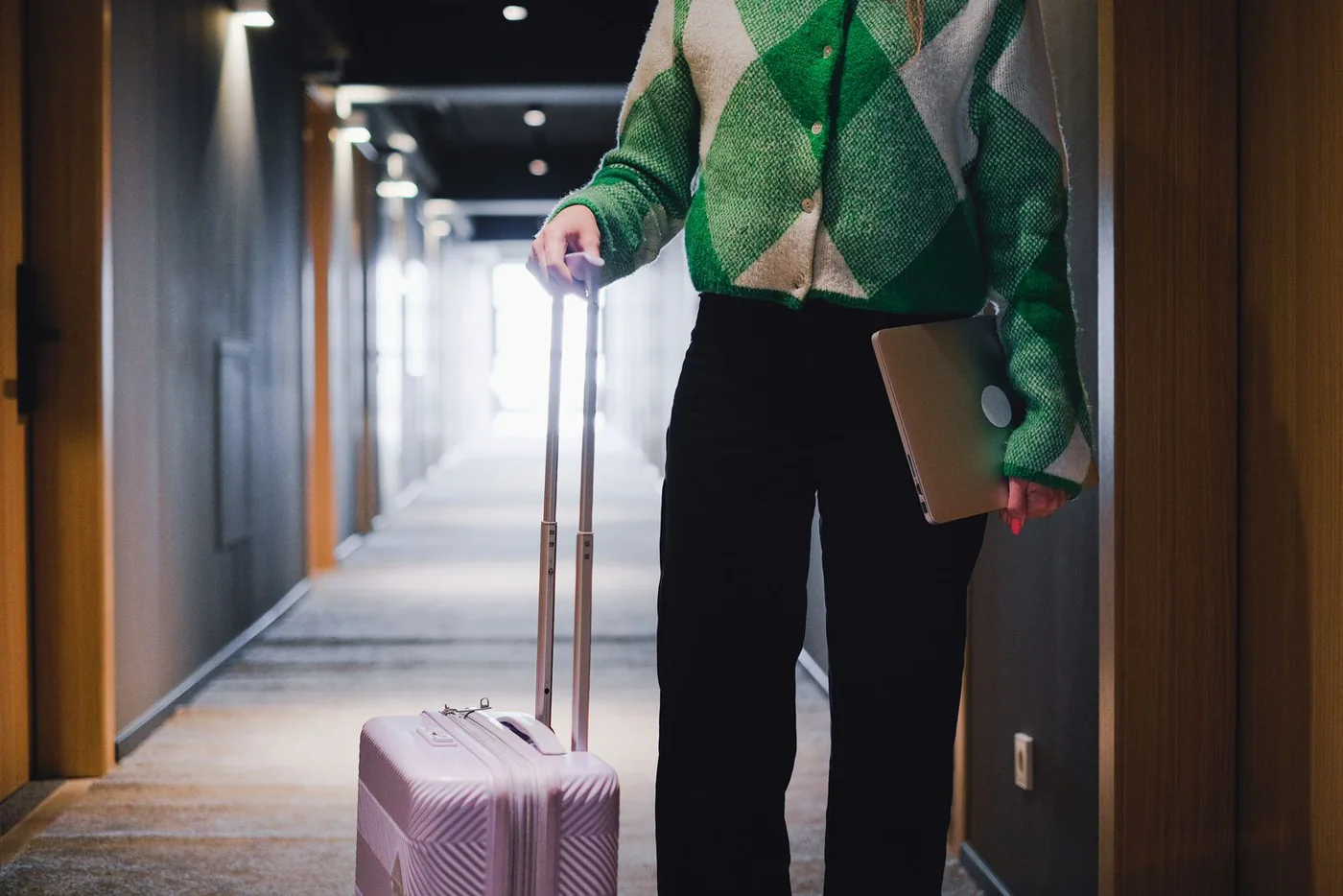 Traveler carrying a laptop and rolling a suitcase through a hotel corridor