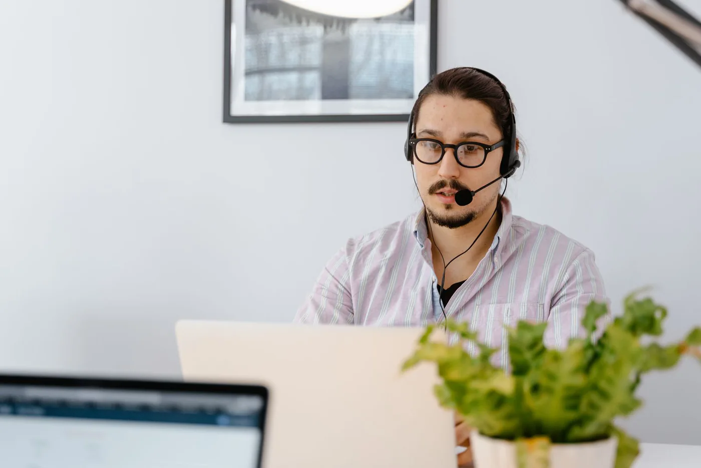 Man wearing a headset while working on a laptop at a home desk